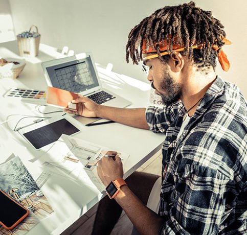 Drawing sketches. Interior designer with dreadlocks wearing red headband drawing sketches